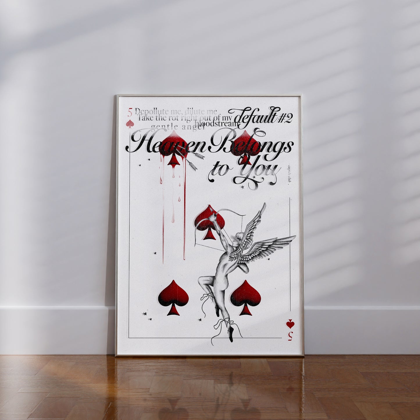 Straight view of 'Heaven Belongs to You’ print laying against a wall. Artwork of Cupid arrow, spade card design, and faded typography.