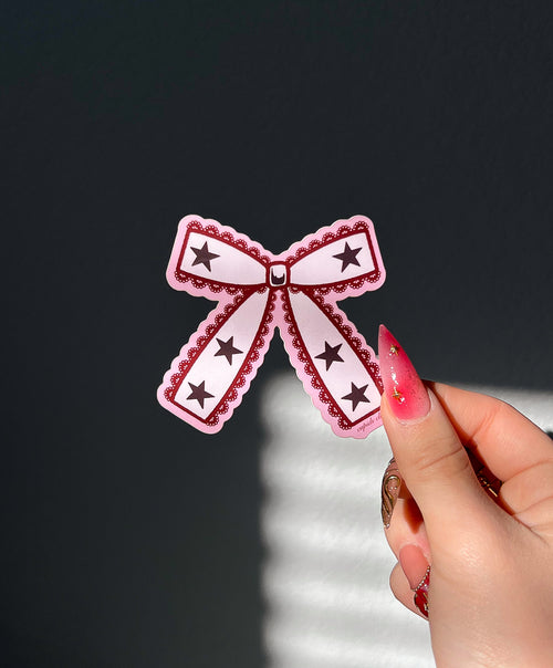 Coquette Lace Bow Sticker in sunlight next to a hand for size comparison