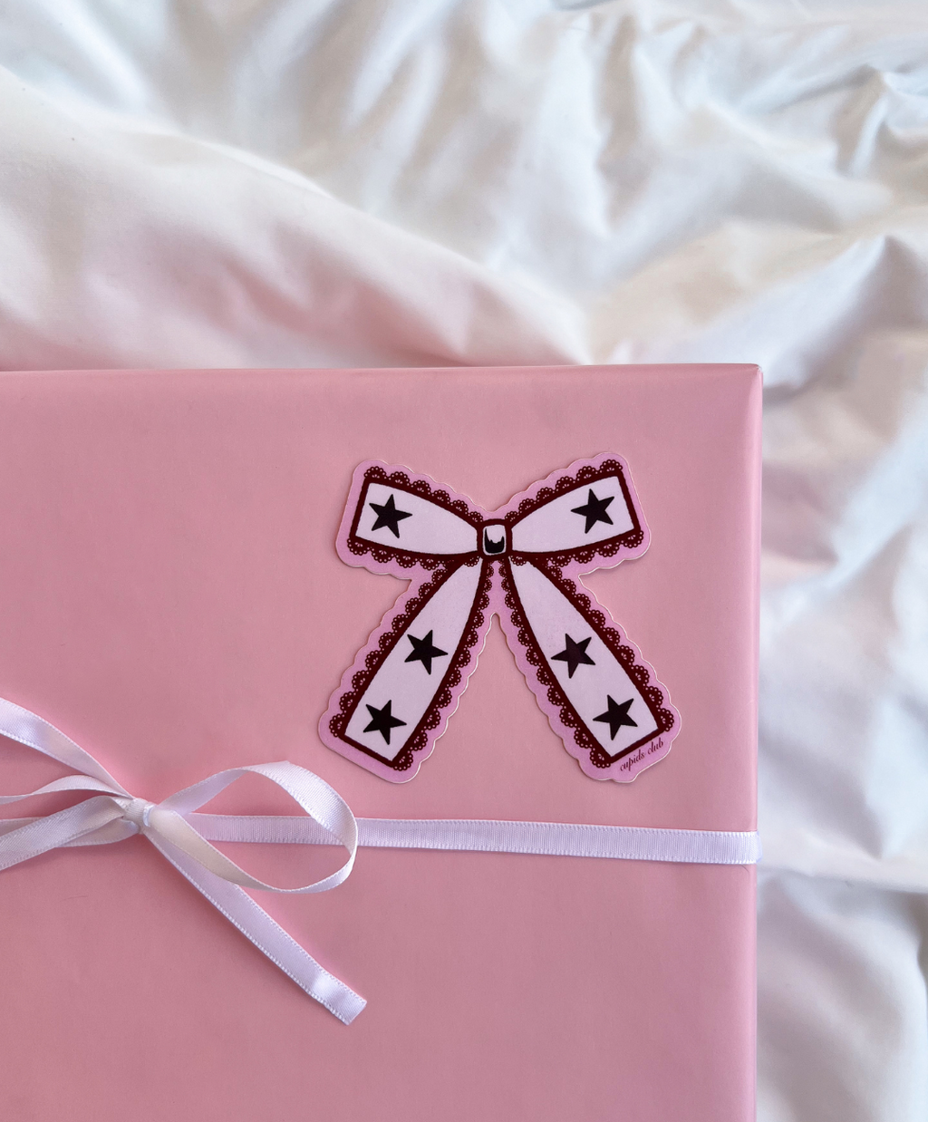 Coquette Lace Bow Sticker on a wrapped pink gift box for size comparison